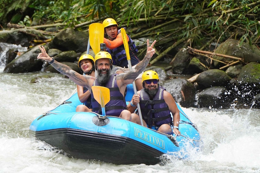 A group of people in a blue inflatable raft with paddles, navigating a river surrounded by rocks and greenery. 4