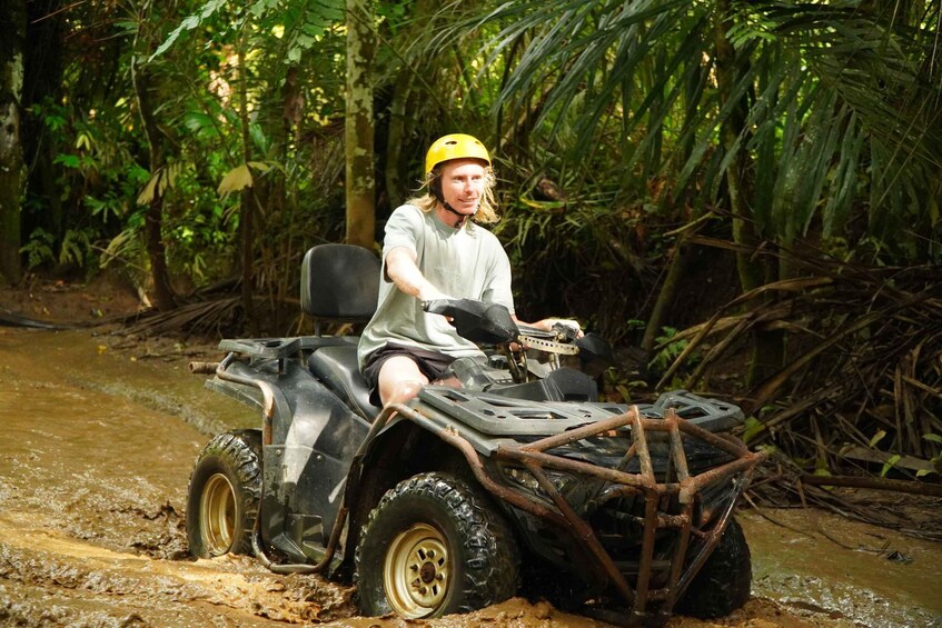 A person riding an ATV in a muddy forest. 3