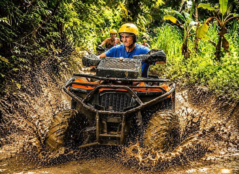 A person driving an ATV through a muddy area with splashing mud. 2