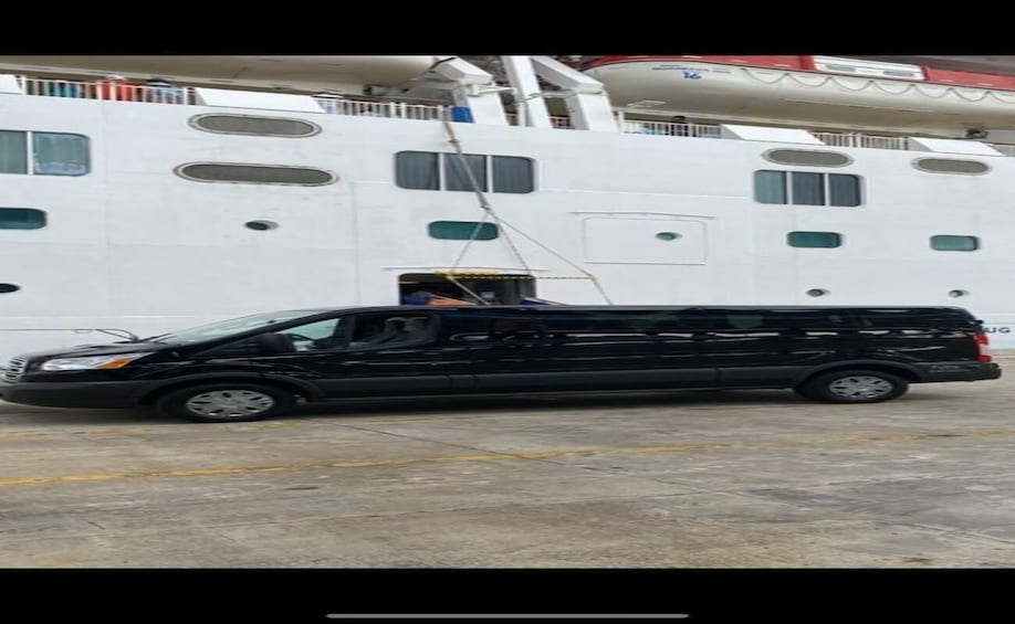 A black van parked in front of a large white ship with multiple windows and a ladder. 5