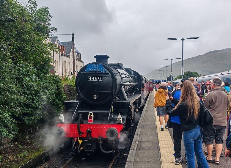 A steam locomotive named 'The Jacobite' with the number 44871, stationary at a station with passengers waiting on the platform. 3