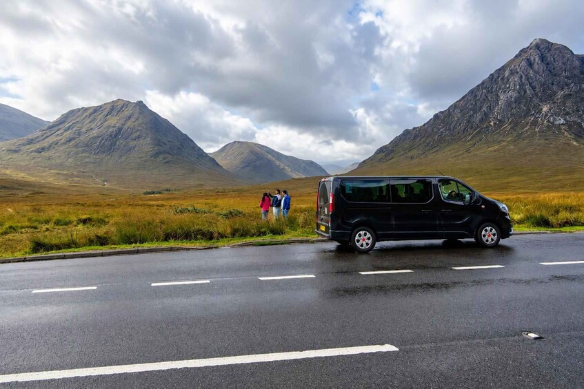 A black van driving on a wet road with a mountainous landscape in the background. 1