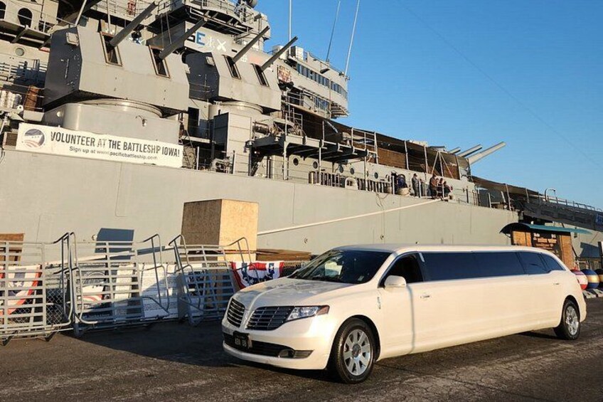 A white SUV parked in front of a large ship with a sign that reads 'VOLUNTEER AT THE BATTLESHIP IOWA'. 1