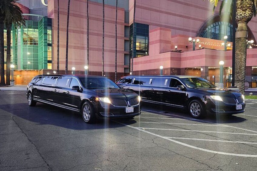 Two black limousines parked in a lot with a modern building in the background. 3