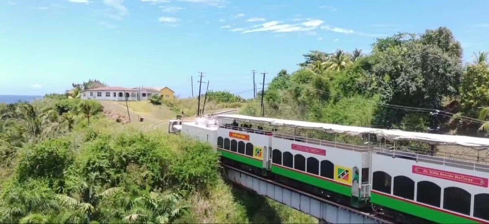 A train on a bridge with greenery and a building in the background. 2