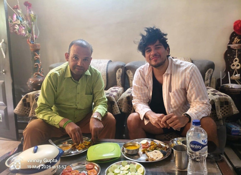 Two men sitting on a couch with plates of food in front of them. 2