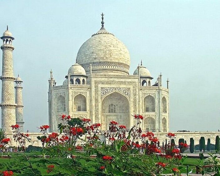 The Taj Mahal with its four minarets and a garden with red flowers. 2