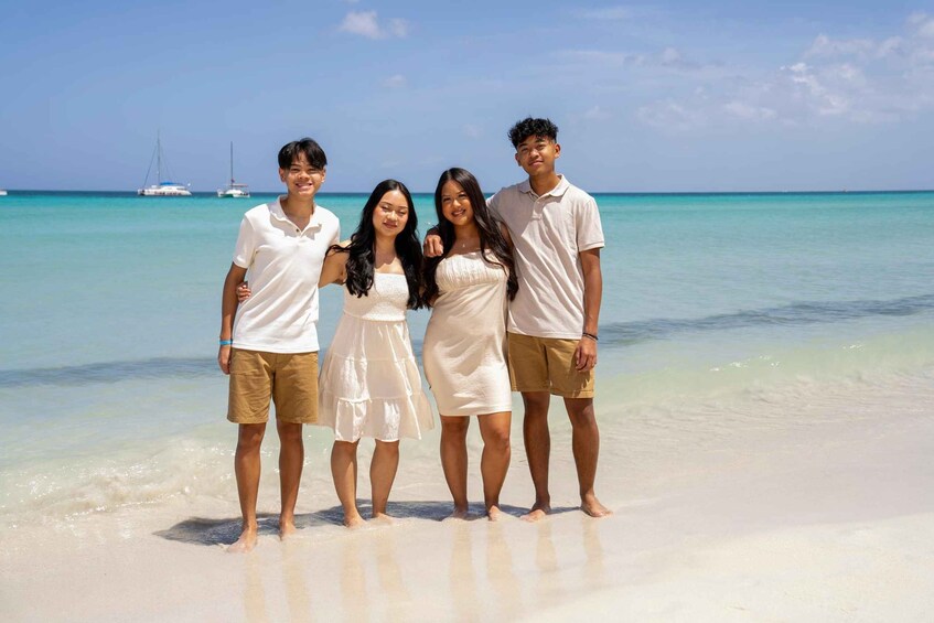 A group of four people standing on a beach with clear turquoise water and boats in the background. 5