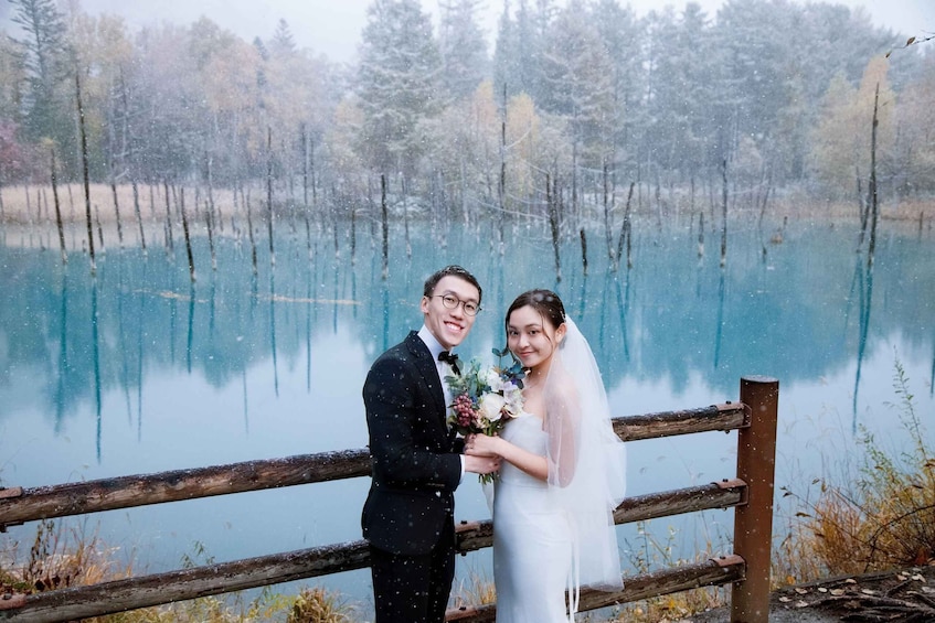A couple standing by a lake with a wooden fence in the foreground. 2