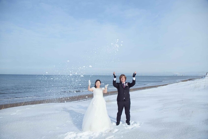 A snowy beach with a wedding couple throwing snow. 1
