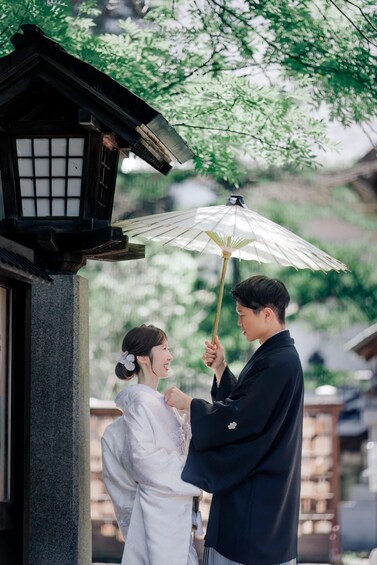 A couple under a traditional Japanese umbrella, standing in front of a building with a lantern. 5