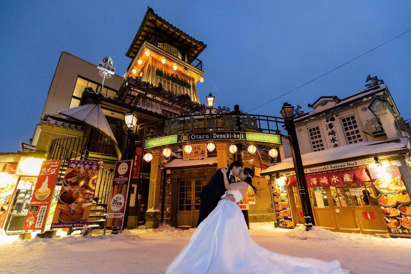 A couple embracing in front of a traditional Japanese building with illuminated signs and snow on the ground. 4