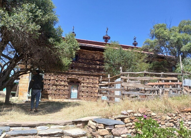 Un edificio de piedra con techo rojo, rodeado de árboles y un muro de piedra. 4