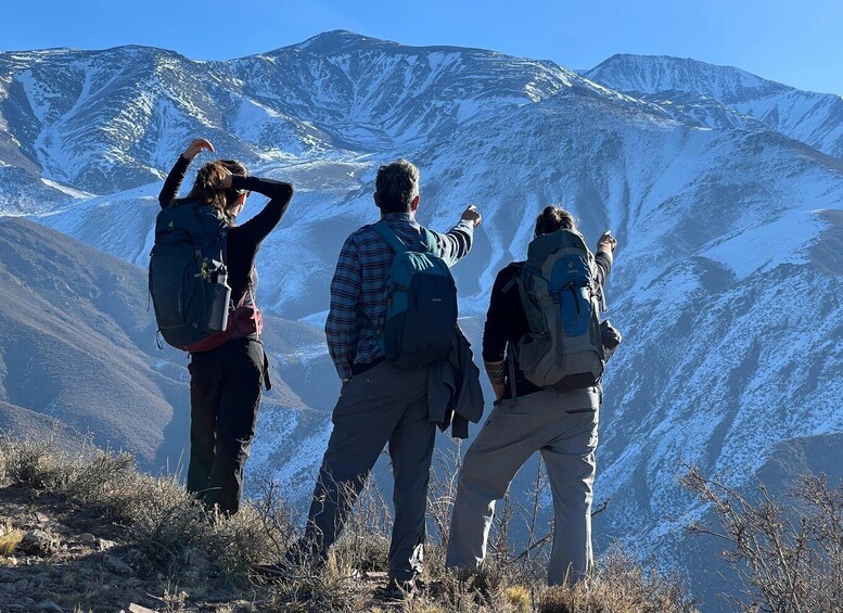 Three hikers on a mountain trail with snow-covered peaks in the background. 1