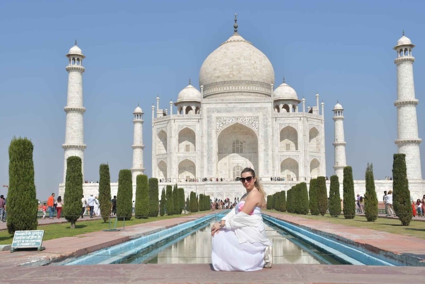 Una persona con un vestido blanco sentada junto a un estanque reflectante, con el Taj Mahal al fondo. 1