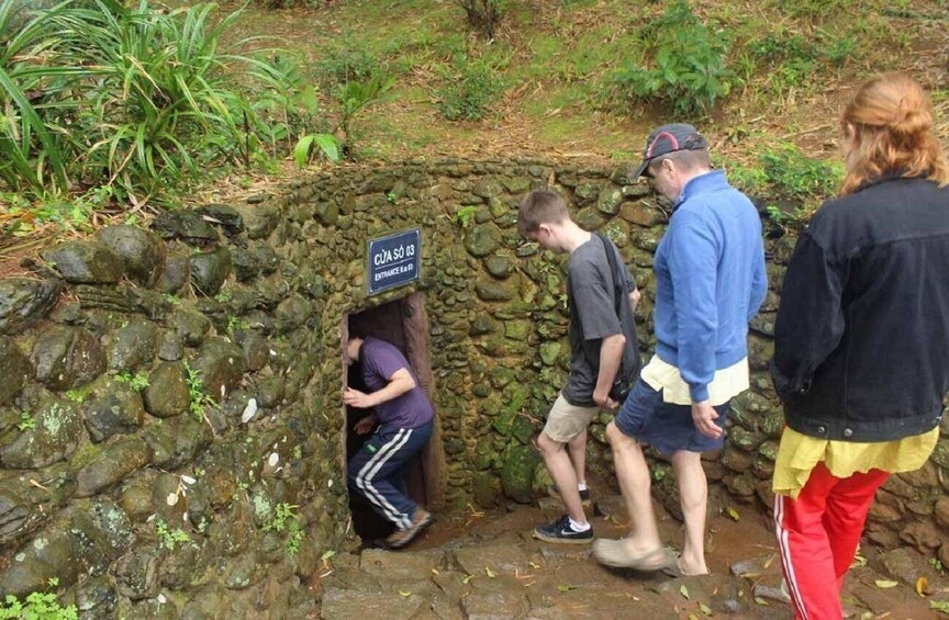 A group of people near a stone wall with a sign that reads "CÚJA SO 03 ENTRANCE R&D." 4
