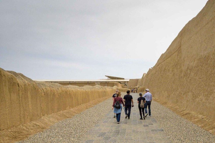 A group of people walking on a gravel path between sand dunes. 2