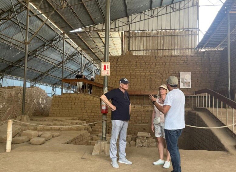A group of people inside a large, open-roofed building with a brick wall and a staircase leading to an upper level. 3