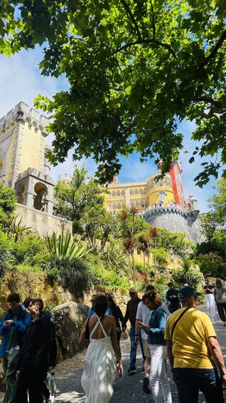 A historic building with arches and a tower, surrounded by lush greenery and people walking. 4