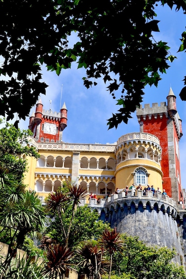 A historic castle with a clock tower, arched windows, and a red and yellow facade. 3