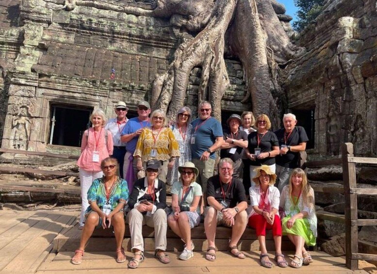 A group of people posing in front of an ancient stone structure with large tree roots. 5