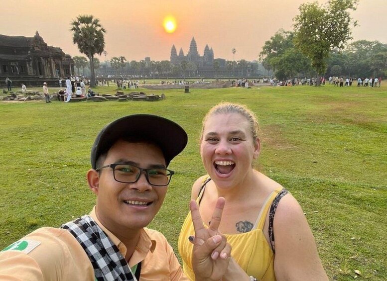 A person in a yellow dress making a peace sign, another person in a cap, and a temple in the background. 2