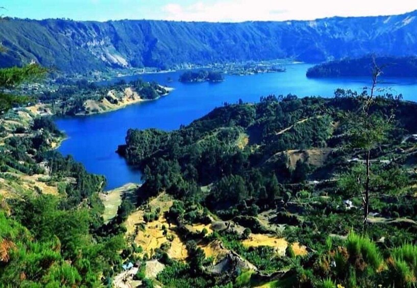 A mountainous landscape with a large lake surrounded by greenery and rugged terrain. 4