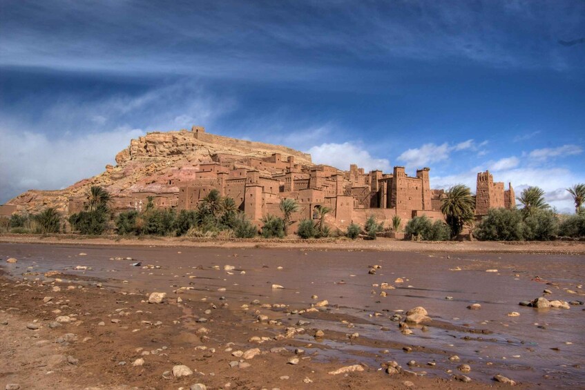 A historic fortified city with ancient architecture, a river in the foreground, and palm trees. 4