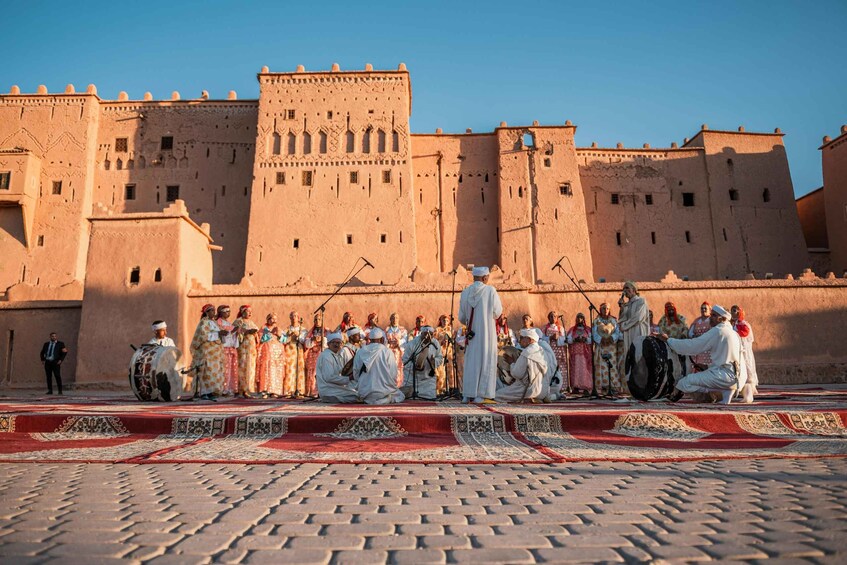 A group of people in traditional attire gathered in front of a large, historic building with a red carpet. 3