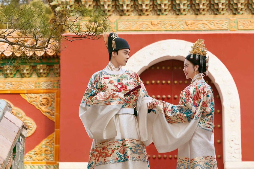 Two people in traditional attire in front of a red building with ornate architecture. 5
