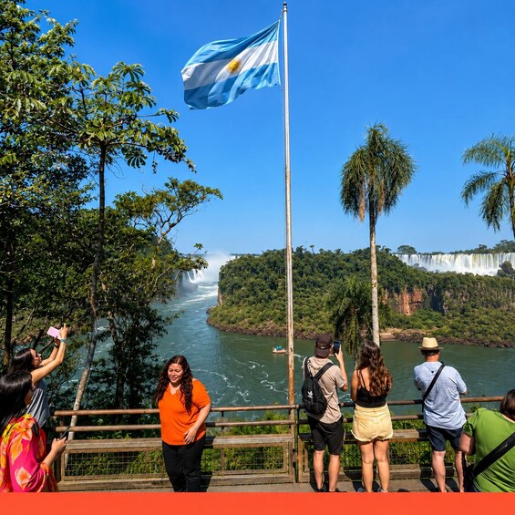 Un grupo de personas tomando fotos cerca de una cascada, con una bandera al fondo. 1