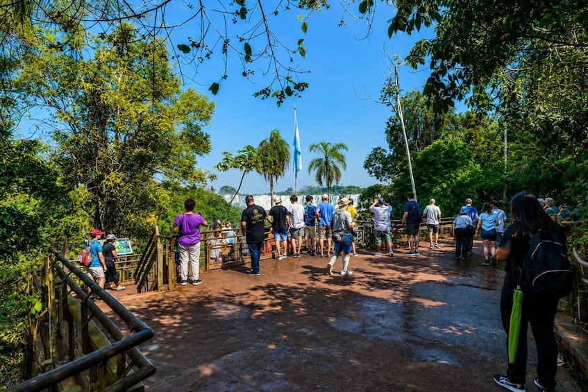A group of people standing on a wet pathway in a tropical forest, looking towards a waterfall. 3