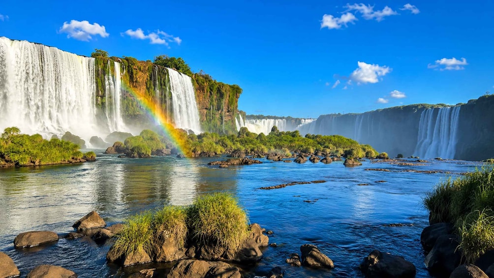 A large waterfall with a rainbow, surrounded by lush greenery and a river. 1