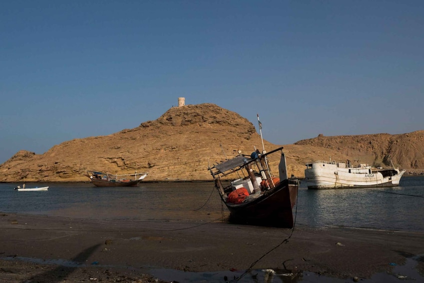 A boat stranded on a sandy beach with a rocky hill in the background. 4