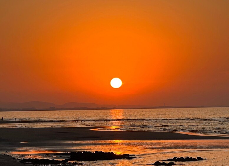 A sunset over a beach with calm waters reflecting the orange sky. 2