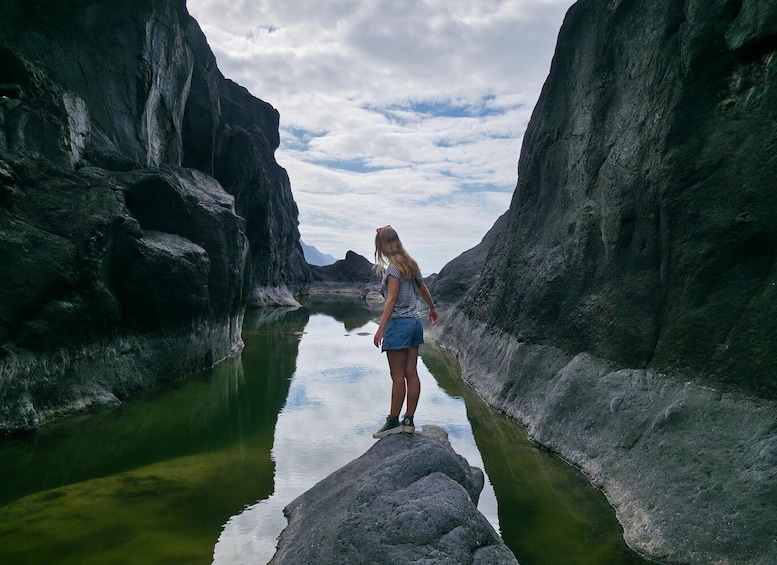 A person standing on a rock by a narrow water channel between steep rock walls. 2