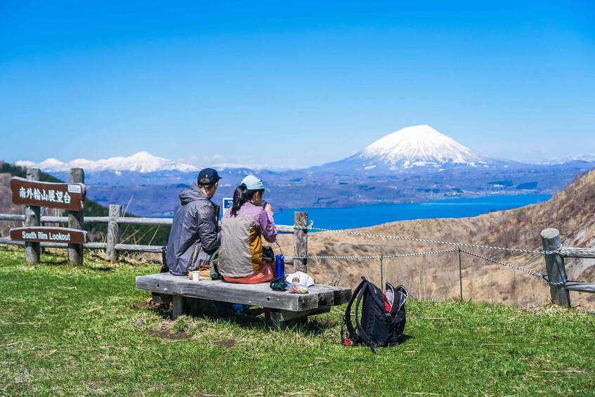 Two people sitting on a bench overlooking a mountain and a lake. 3