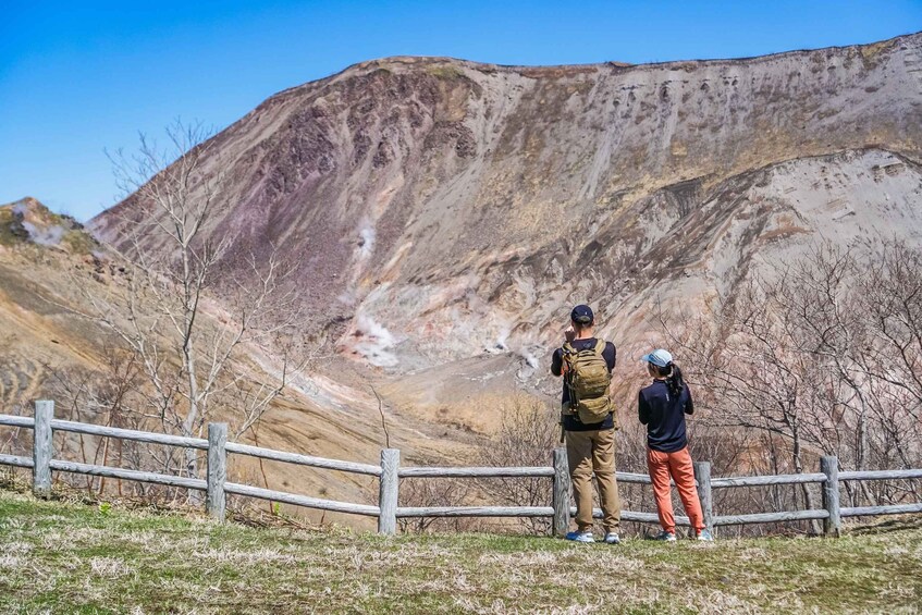 Two people standing by a wooden fence overlooking a mountainous landscape. 4
