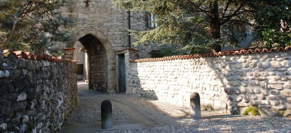 A stone pathway leading to an arched doorway, surrounded by stone walls and trees. 3