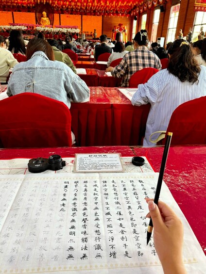 A person holding a traditional brush, writing Chinese calligraphy on a paper placed on a table. 1