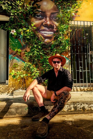 A man sitting on steps in front of a mural, wearing a hat and sunglasses. 5