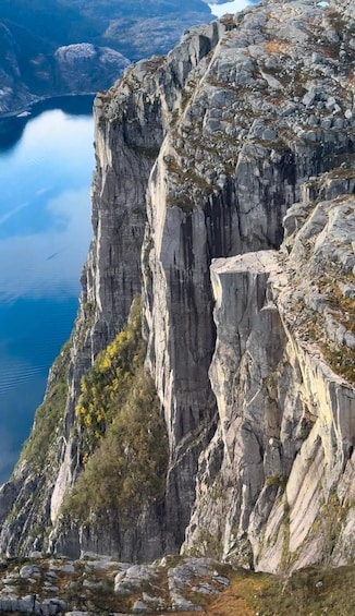 A rugged mountain cliff with a steep drop overlooking a calm lake. 1