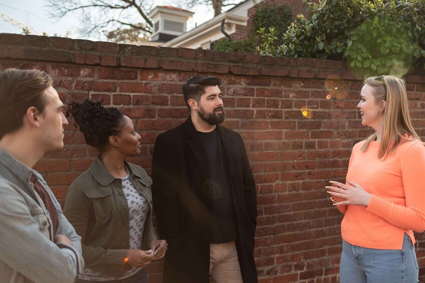 Four people standing outdoors against a brick wall. 2