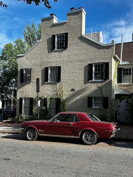 A red vintage car parked in front of a stone building with black shutters. 3