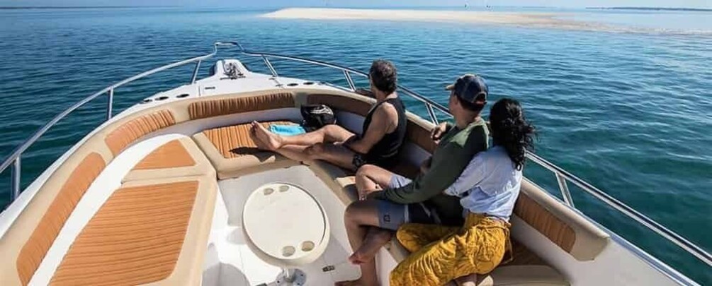 A boat with three people on board, a sandy beach in the background, and calm waters. 2