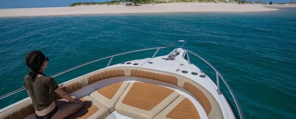 A boat with a person on the bow, a sandy beach, and clear blue water. 5