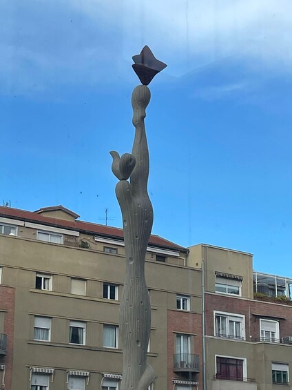 A tall, abstract sculpture with a star-like top, set against a backdrop of residential buildings. 2