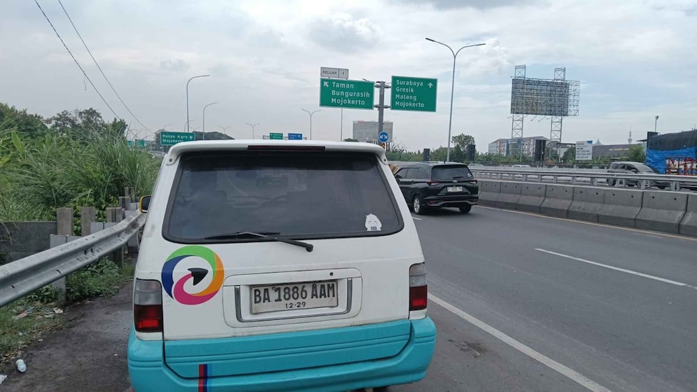 A white van with a colorful logo on the back, parked on the side of a highway. 4