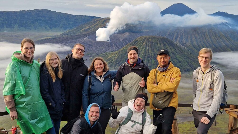 A group of people standing in front of a mountainous landscape with a volcano emitting smoke. 3