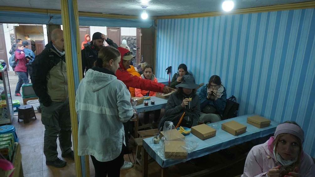 A group of people gathered around a table with food boxes, some are eating while others are standing. 2